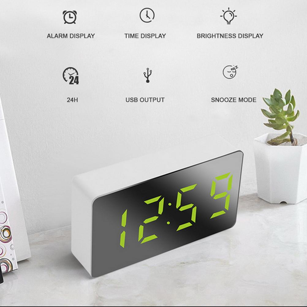 Eine Digitaluhr zeigt 12:59 in Grün an. Symbole oben zeigen Alarm, Zeit, Helligkeit, 24h, USB und Schlummermodus. Rechts eine kleine Pflanze.