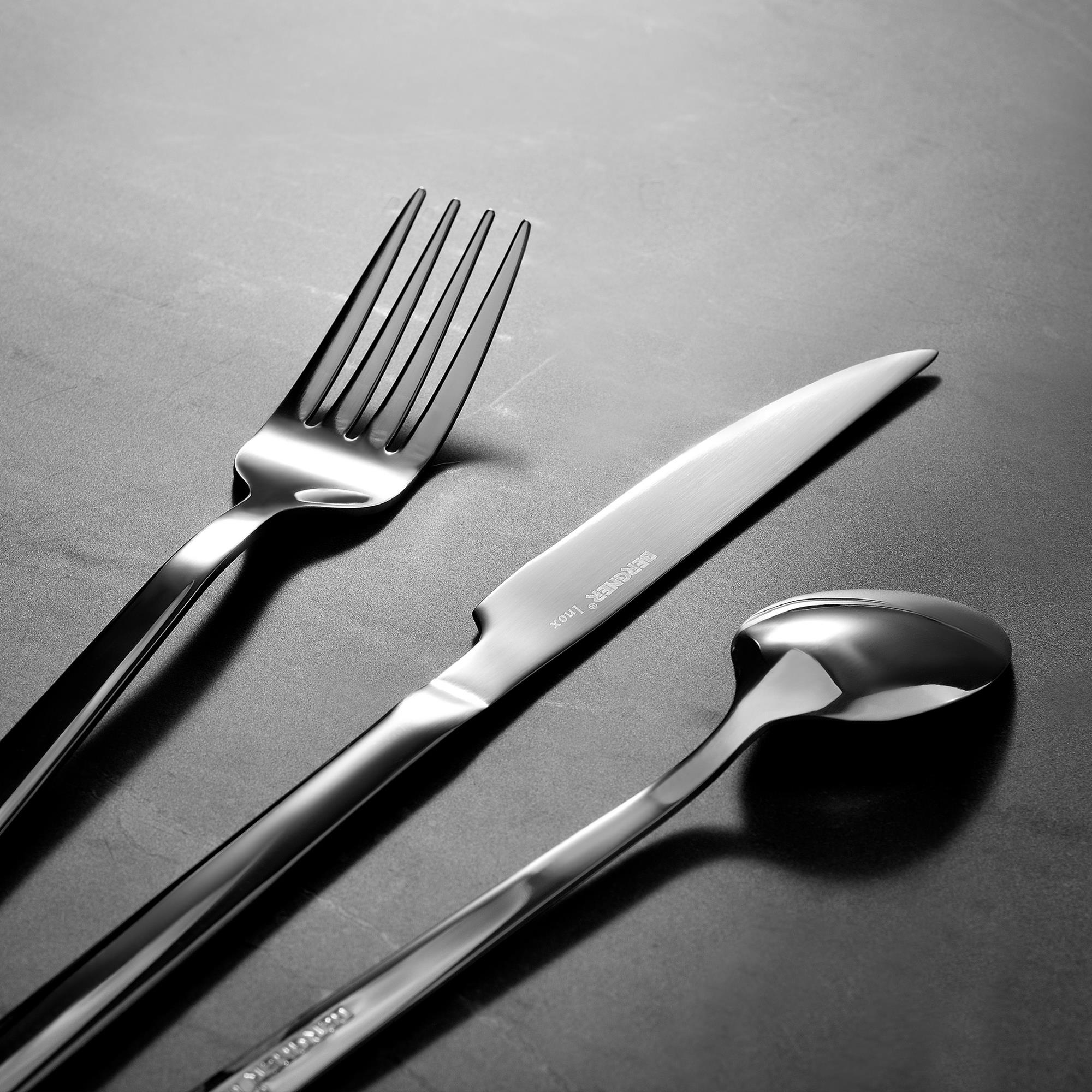 Primer plano de cubiertos, incluyendo tenedor, cuchillo y cuchara, todos de metal brillante, sobre una superficie oscura.