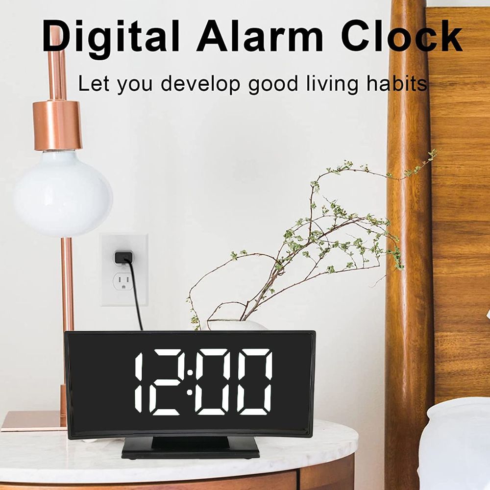 Digitaler Wecker, der 12:00 Uhr anzeigt, auf einem Nachttisch mit Lampe, Pflanze und einem Teil eines Bettes.