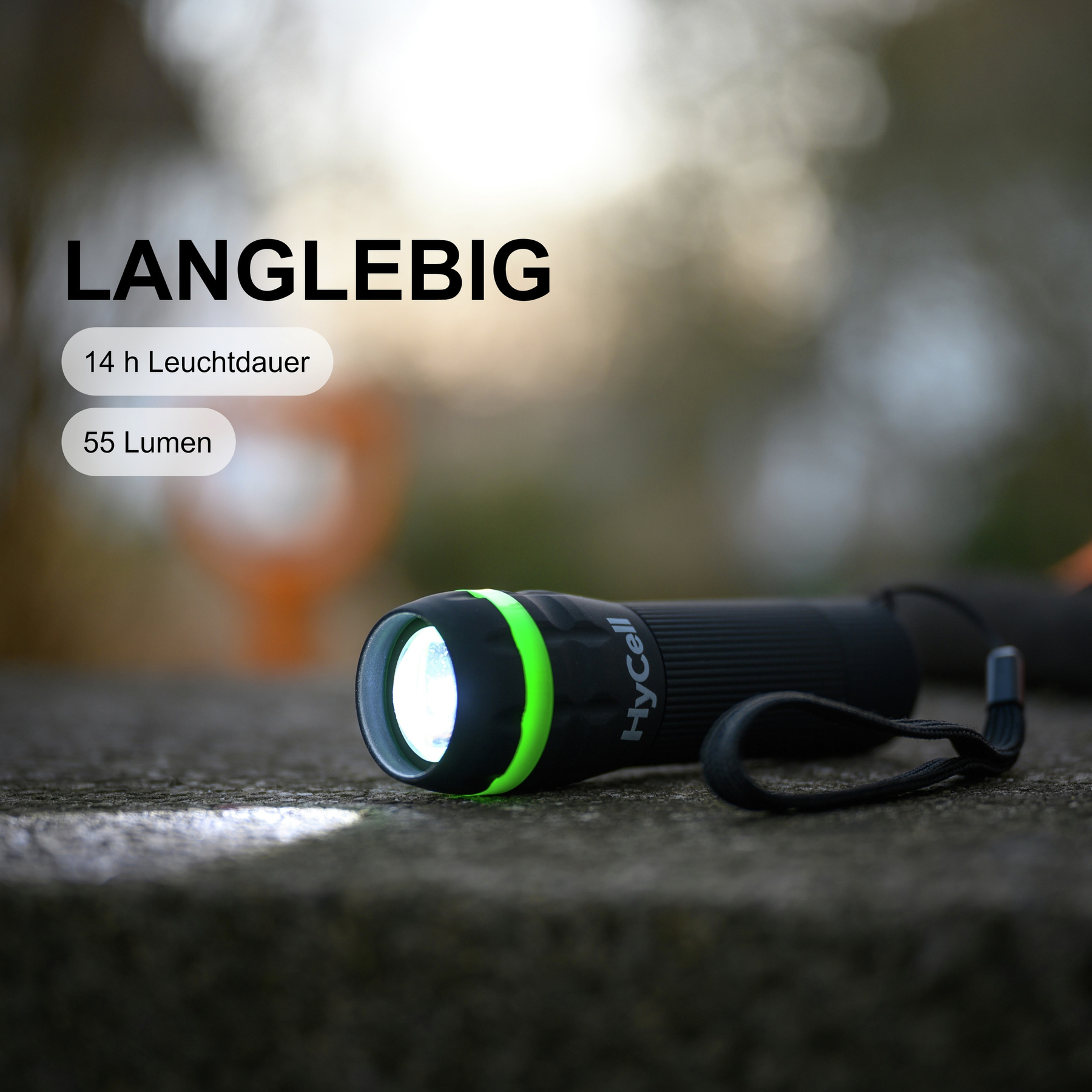 Une lampe de poche noire et verte est sur une surface texturée. La lumière est allumée. Le fond est flou avec le mot Langlebig.