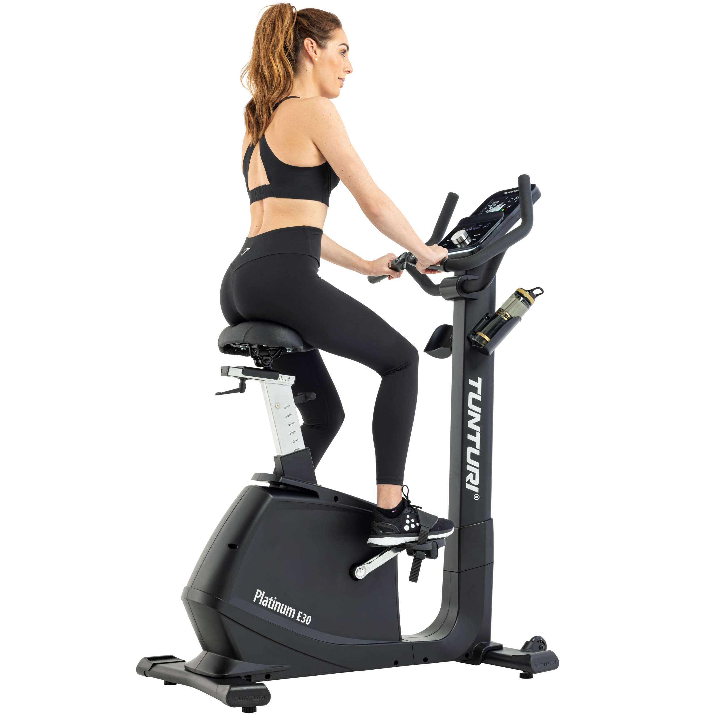 Een vrouw in zwarte sportkleding traint op een zwarte hometrainer. De merknaam 'Tunturi' is zichtbaar.