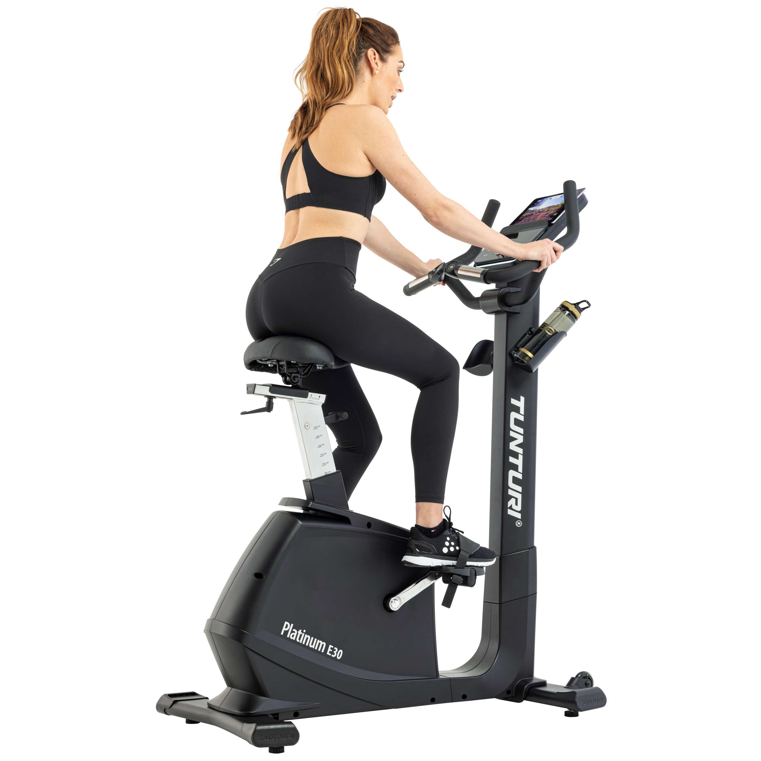 Een vrouw traint op een zwarte hometrainer. Ze draagt zwarte sportkleding. De fiets is zwart, met een waterfles.