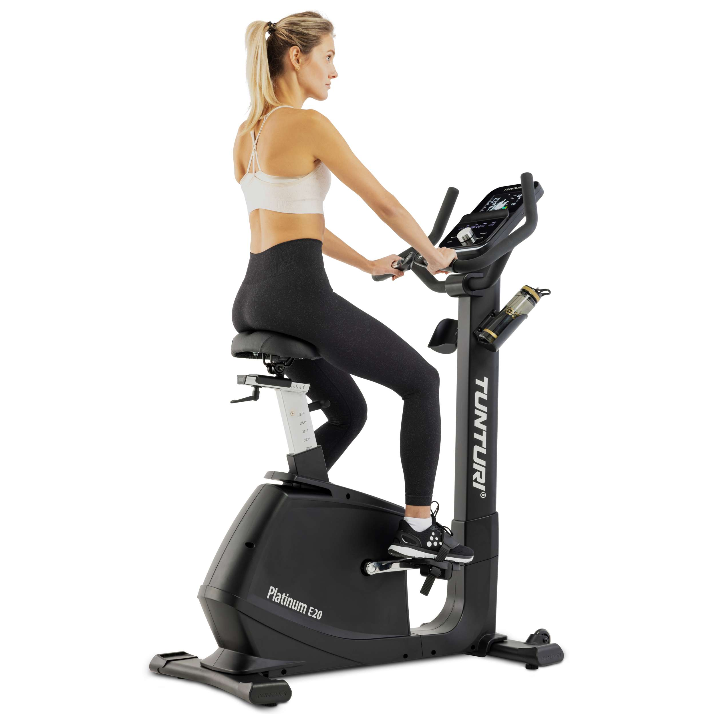 Een vrouw in sportkleding traint op een zwarte hometrainer. Ze is blond en heeft een paardenstaart.