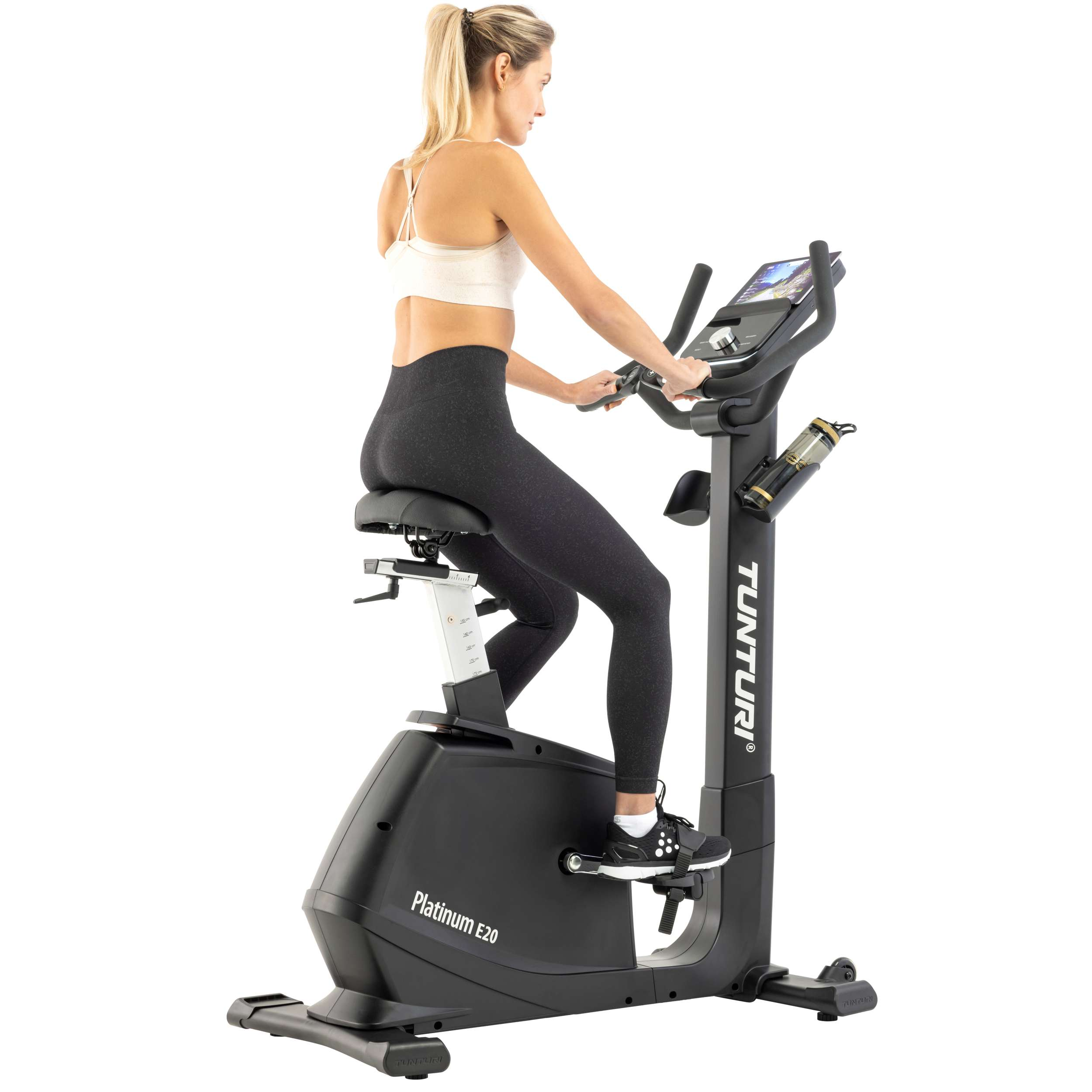 Blonde vrouw die op een zwarte hometrainer traint. Ze draagt een witte sport-bh en zwarte leggings.