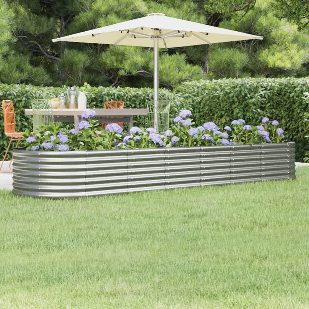 Eine Gartenszene mit einem Metallpflanzer mit blauen Blumen, einem Tisch, Stühlen und einem Sonnenschirm auf einer Wiese.