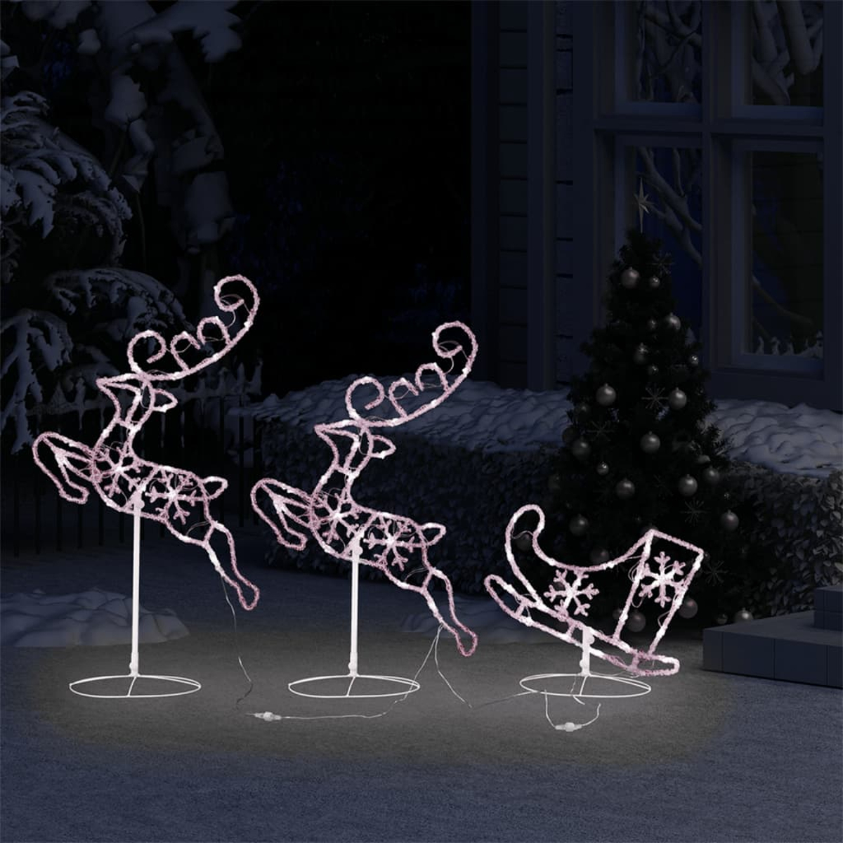 Beleuchtete Rentier- und Schlittendekoration im Freien bei Nacht. Ein Weihnachtsbaum befindet sich im Hintergrund. Schnee liegt auf dem Boden.