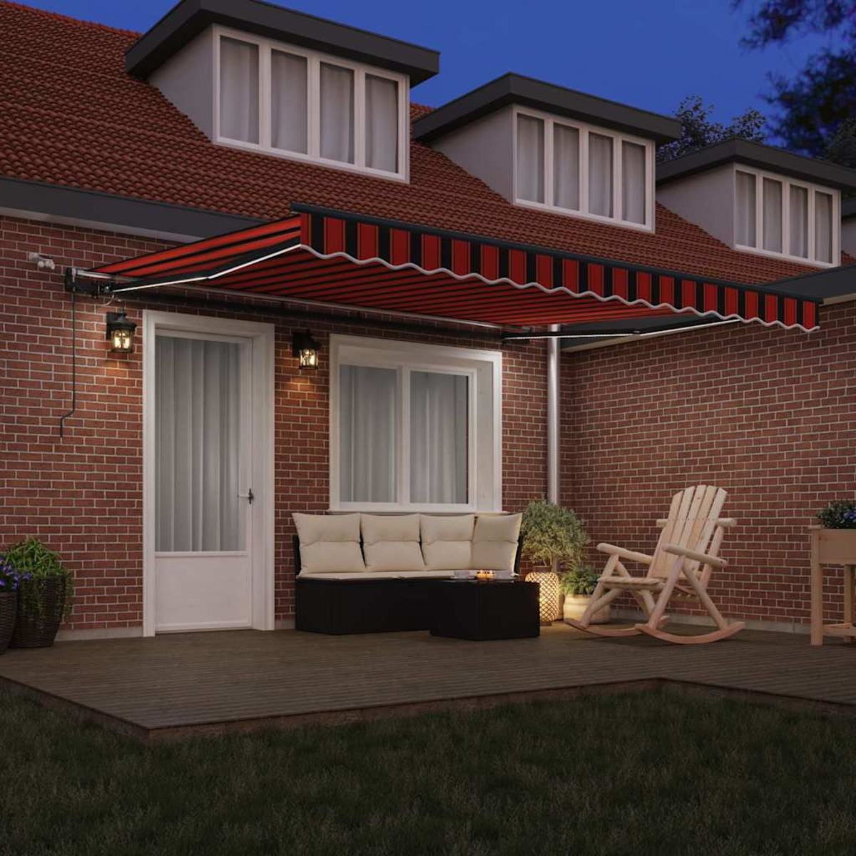 Hausfassade in der Dämmerung. Eine rot-schwarz gestreifte Markise bedeckt eine Terrasse mit Möbeln und einem Schaukelstuhl. Ziegelmauern.