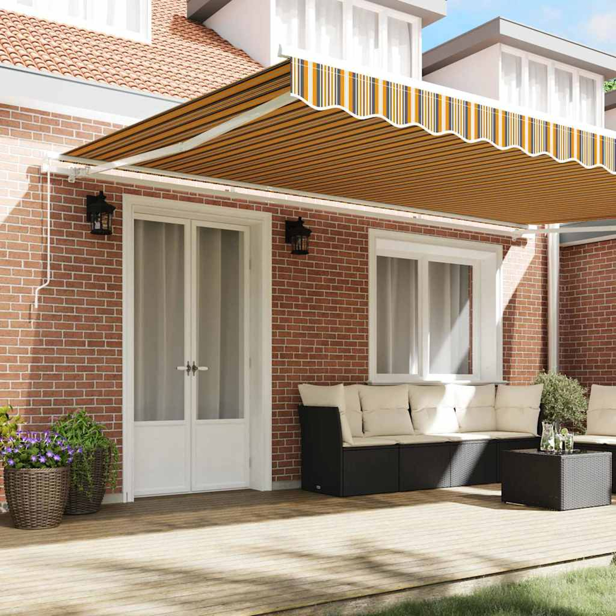 Una casa con toldo. Un sofá, mesa y plantas en terraza de madera. Pared de ladrillo con puerta y ventanas.