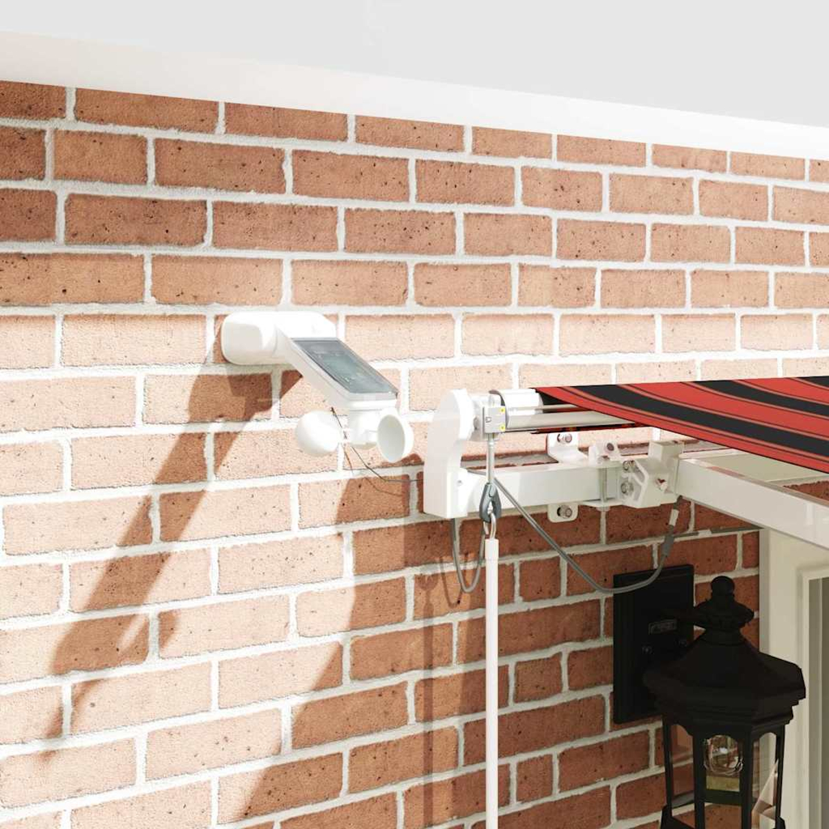 Eine Backsteinmauer mit weißen Vorrichtungen, eine gestreifte Markise und eine schwarze Laterne. Die Wand hat ein weißes Solarpanel und einen Sensor.