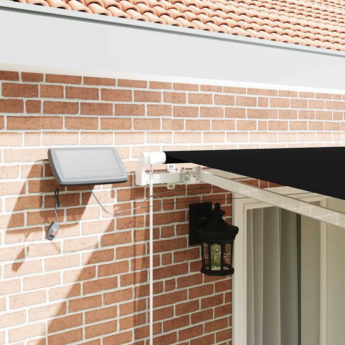 Ziegelmauer mit schwarzer Markise, Solarpanel, Lampe und weißer Struktur. Rotes Ziegeldach im Hintergrund.