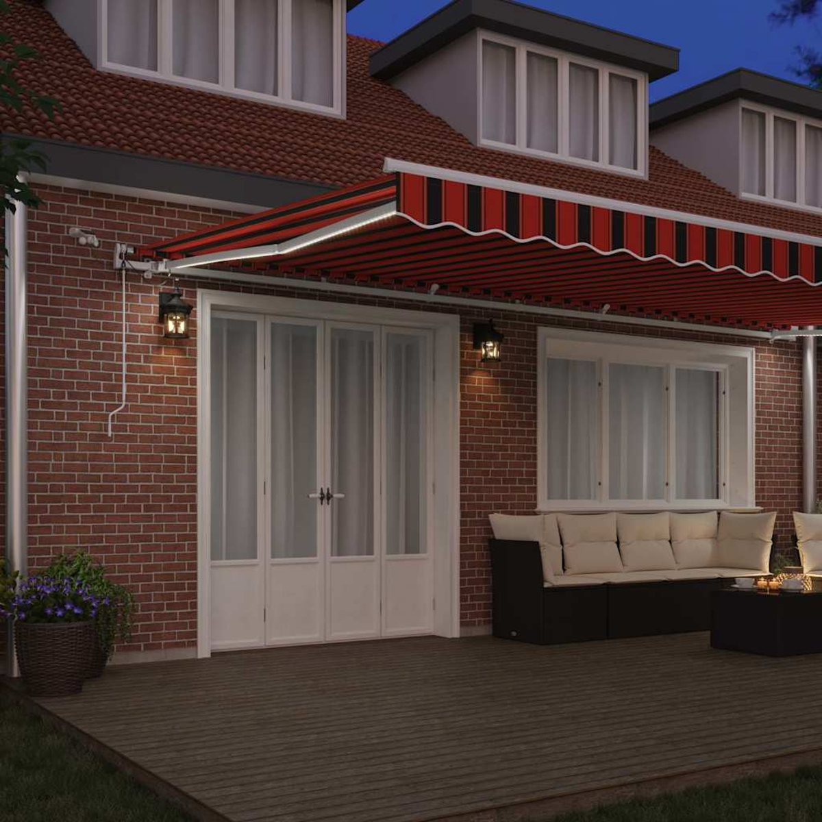 Ein Haus mit einer rot-schwarz gestreiften Markise. Es gibt eine Holzterrasse, ein Sofa und einen Tisch. Das Haus hat Ziegelmauern und weiße Türen.