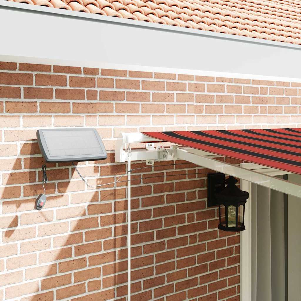 Eine Ziegelmauer mit einem Solarpanel, eine Markise mit rot-schwarzen Streifen und eine Laterne.