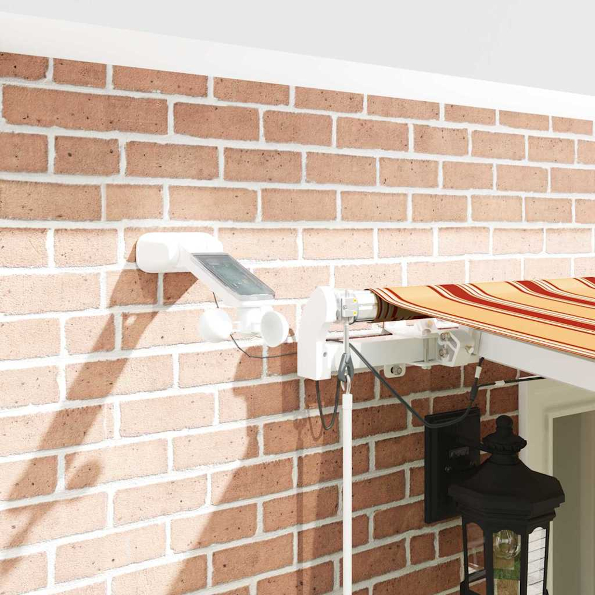 Ziegelmauer mit weißem Markisensystem. Ein Solarpanel und eine schwarze Laterne sind an der Wand befestigt.