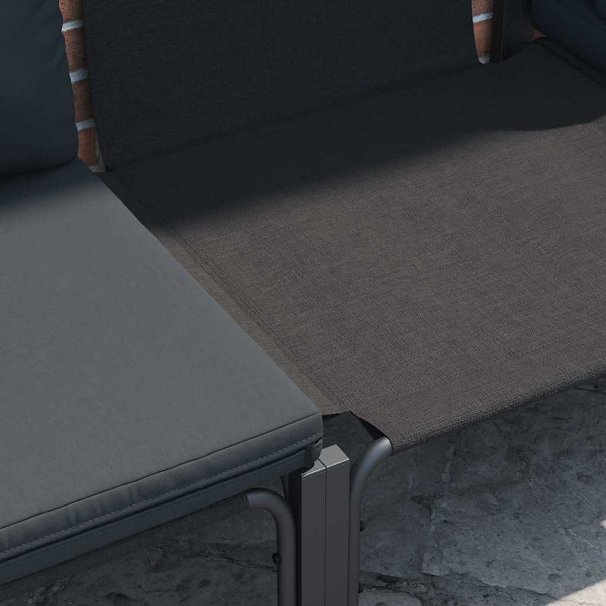 Primo piano di mobili da esterno. Cuscino grigio scuro, tessuto a rete grigio scuro e muro di mattoni. I mobili sono su una superficie di pietra.