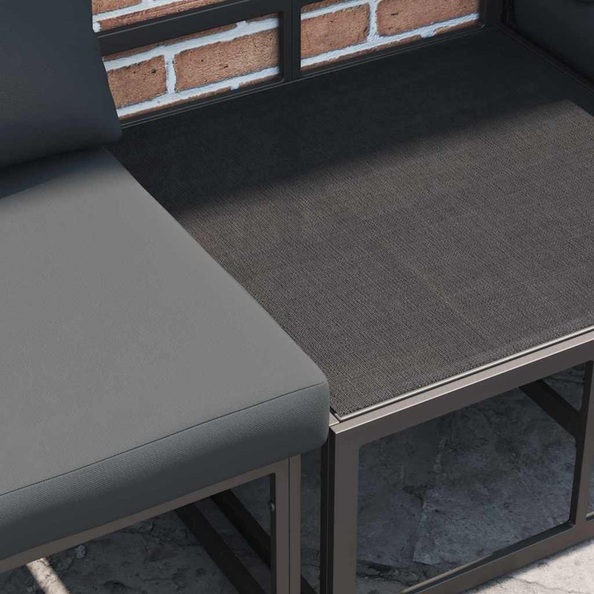 Primo piano di un'area salotto moderna all'aperto. Presenta cuscini grigi, tavolo strutturato grigio scuro e sfondo di muro di mattoni.