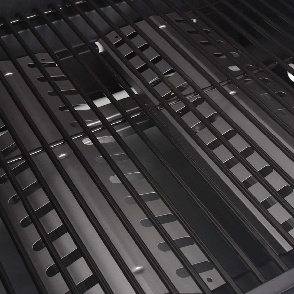 Nahaufnahme eines schwarzen Grillrosts. Parallele Metallstangen mit rechteckigen Aussparungen verlaufen über das Bild und bilden ein gitterartiges Muster.