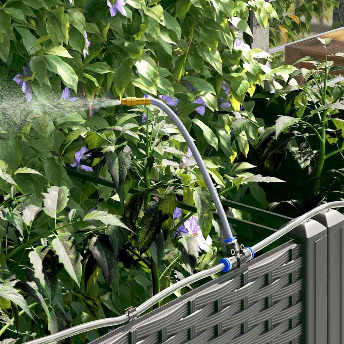 Un irrigatore da giardino spruzza acqua su piante verdi e fiori viola, con una recinzione grigia in primo piano.