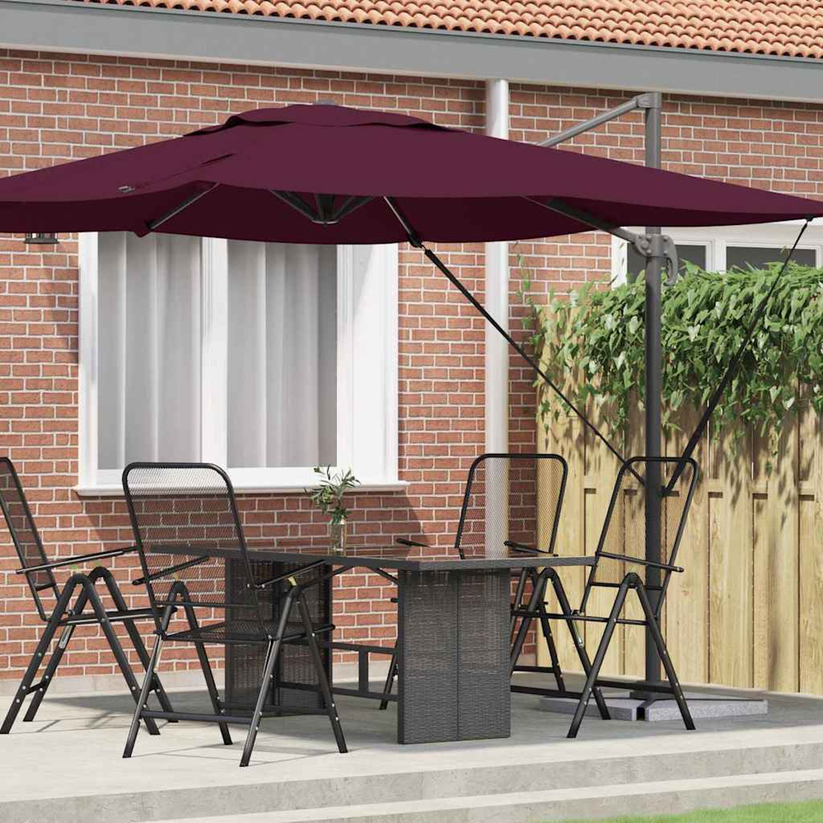 Scena del patio: ombrellone bordeaux, tavolo, sedie. Muro di mattoni rossi sullo sfondo con finestra. Recinzione in legno con piante verdi.