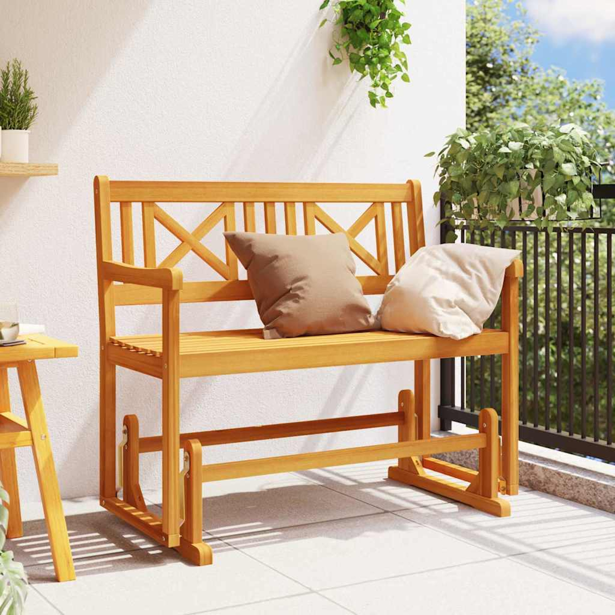 Panca in legno con cuscini su un balcone. Ci sono piante intorno e un muro bianco.