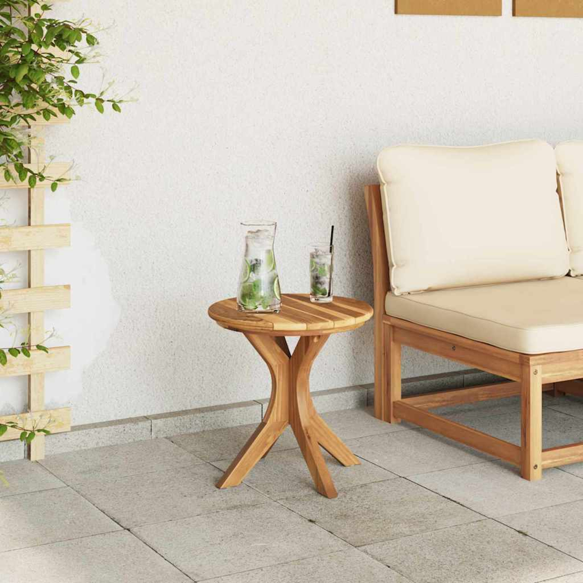 Ein Holztisch mit einem Glaskrug und einem Glas Getränk, neben einer Holzbank mit cremefarbenen Kissen auf einer Terrasse.