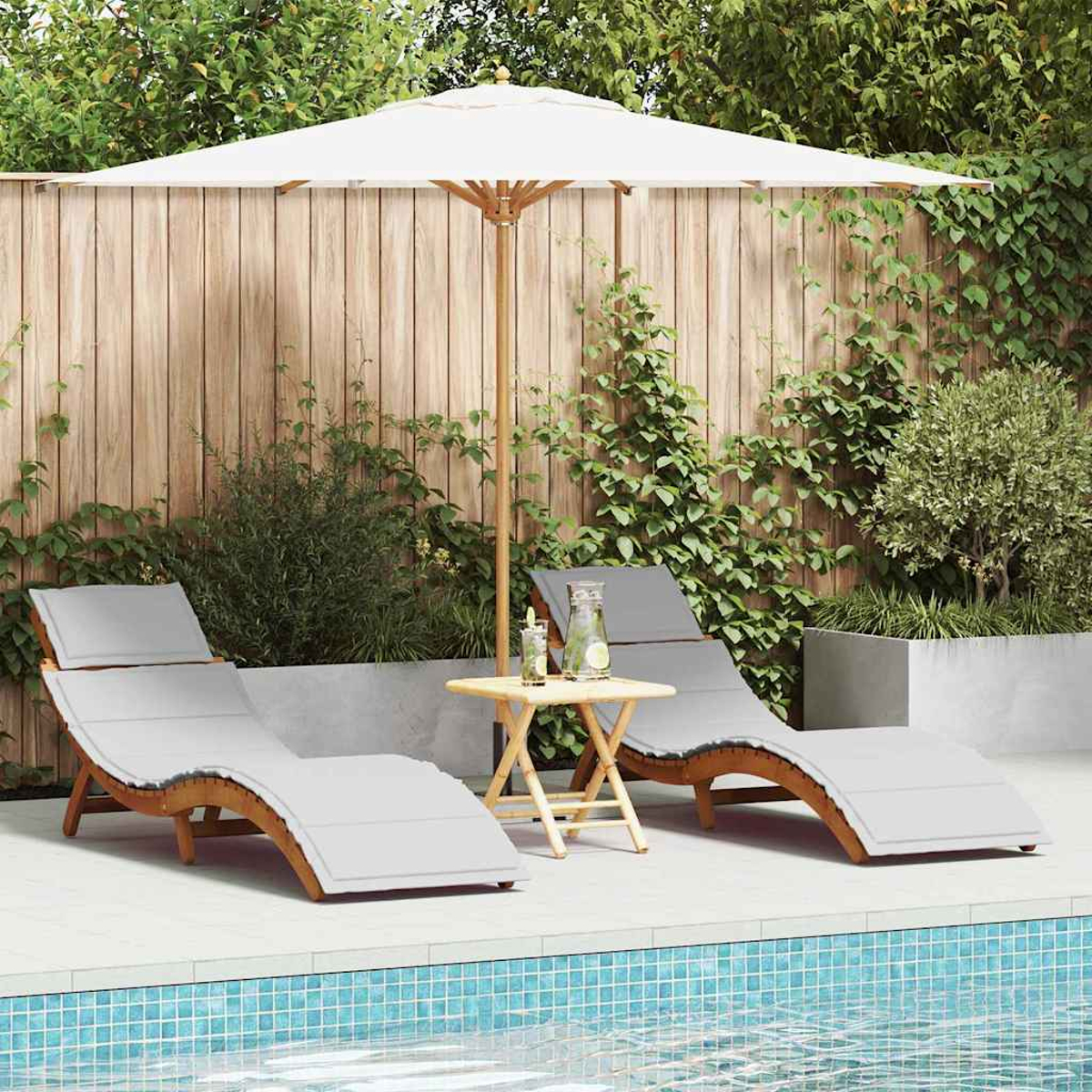 Zwei Liegestühle mit grauen Kissen unter einem weißen Sonnenschirm neben einem Pool. Ein kleiner Tisch hält Getränke. Grüne Pflanzen umgeben.