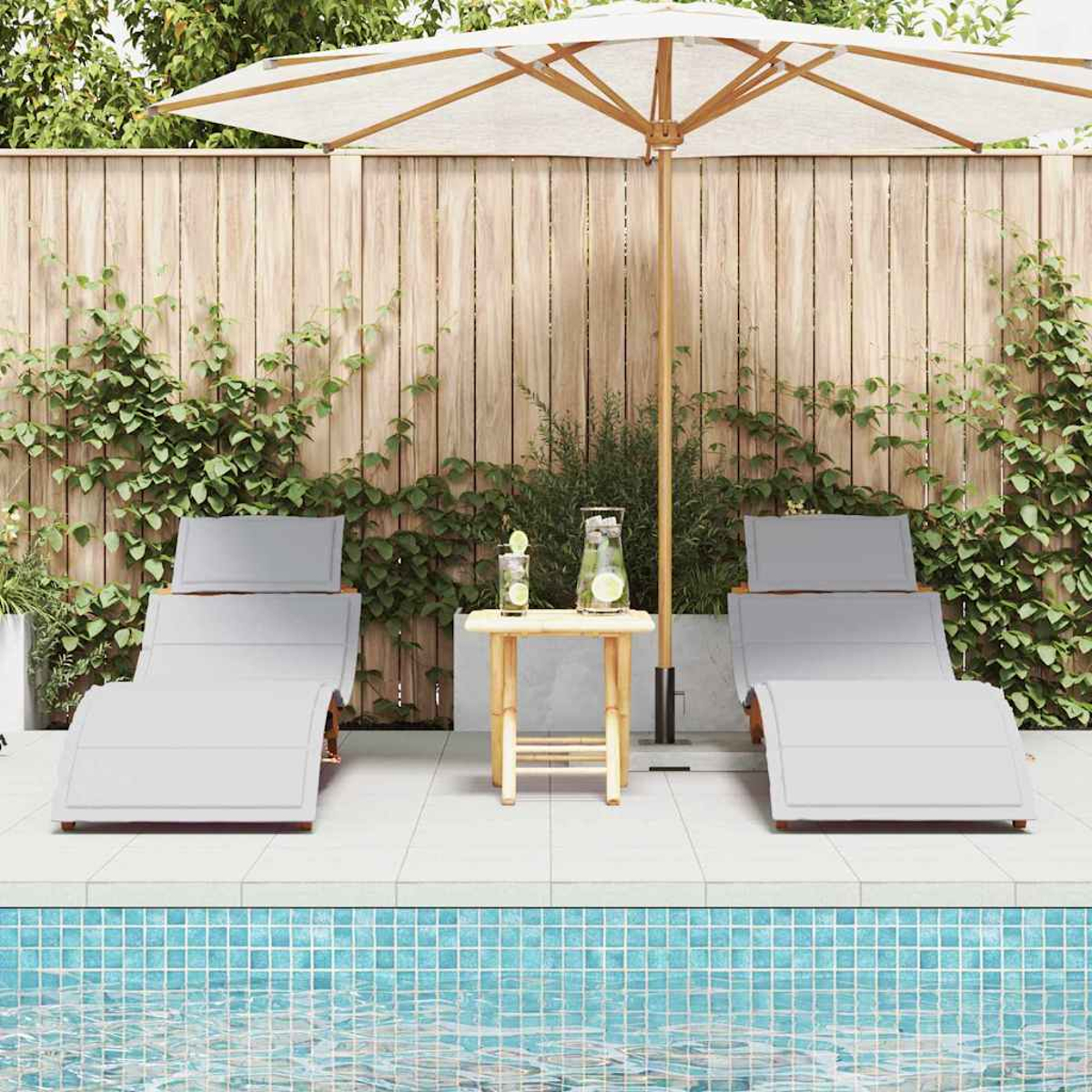 Zwei graue Liegestühle mit einem kleinen Tisch, Getränken und einem Sonnenschirm in der Nähe eines Pools. Im Hintergrund ist ein Holzzaun.