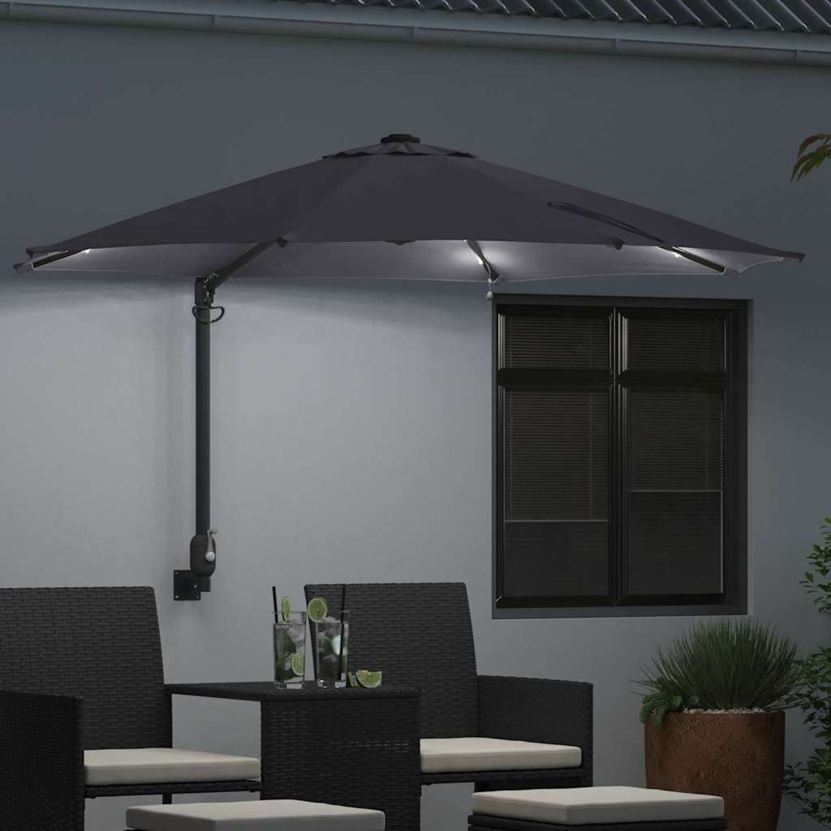 Scena del patio all'aperto con un ombrello grigio scuro con luci. Due sedie in vimini e un tavolo, bevande e una finestra sullo sfondo.