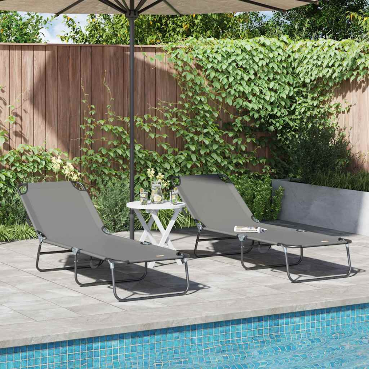 Zwei graue Liegestühle neben einem kleinen weißen Tisch, in der Nähe eines Pools. Grünes Laub und ein Holzzaun sind im Hintergrund.