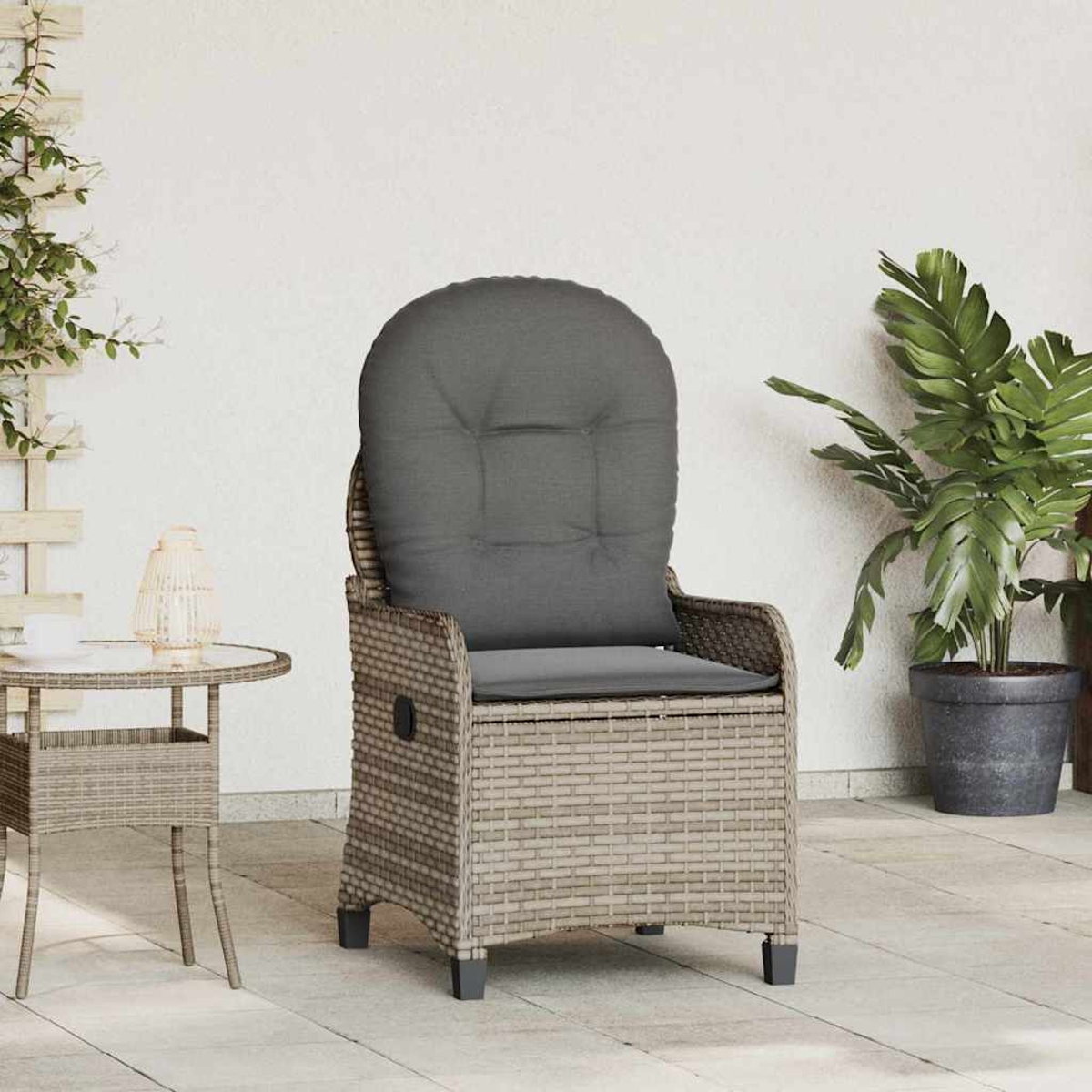 Ein Rattanstuhl mit grauem Kissen steht auf einer Terrasse. Ein Tisch und eine Pflanze stehen neben dem Stuhl. Weiße Wand im Hintergrund.