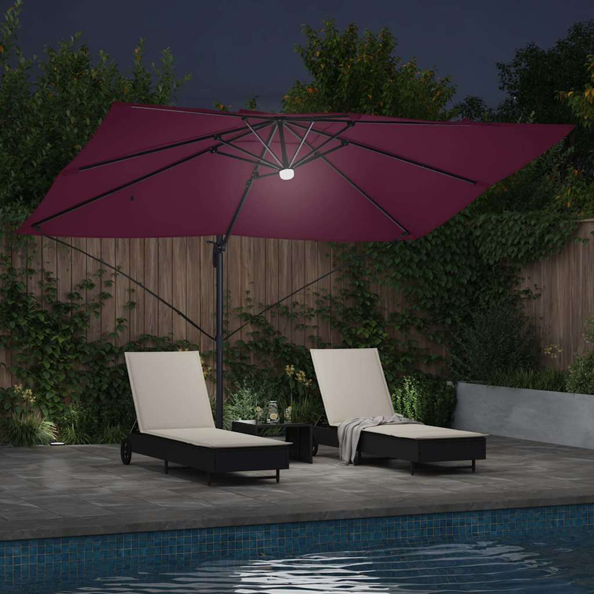 Una scena del patio di notte con due sedie a sdraio sotto un ombrello bordeaux. Sono visibili anche un tavolino e una piscina.