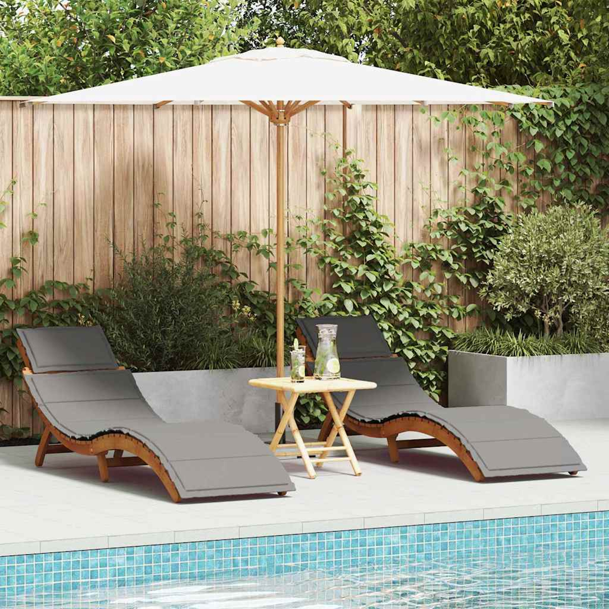 Dos tumbonas, una mesa y una sombrilla junto a una piscina. Plantas verdes y una valla de madera al fondo.