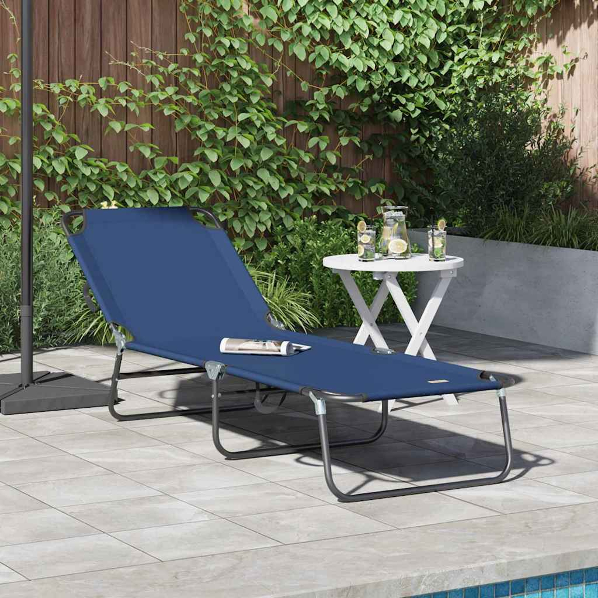 Ein blauer Liegestuhl mit einer Zeitschrift steht auf einer Terrasse neben einem weißen Tisch mit Getränken und Grünpflanzen. Im Hintergrund ein Holzzaun.
