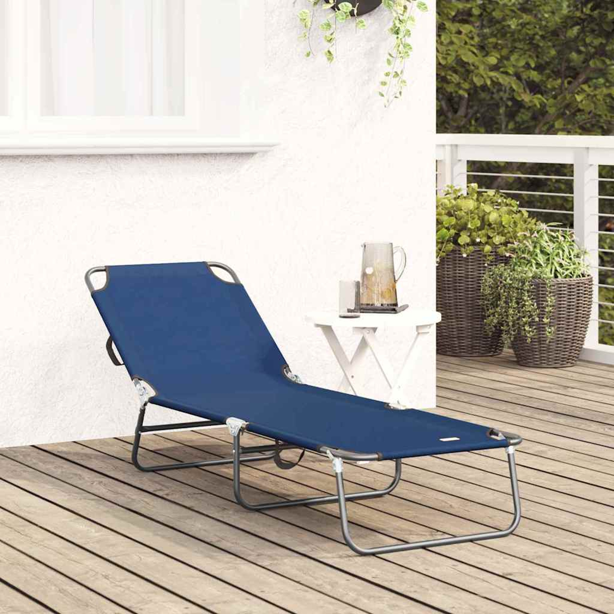 Ein blauer Liegestuhl auf einer Holzterrasse. Daneben ein kleiner Tisch mit Krug und Gläsern. Im Hintergrund Pflanzen.