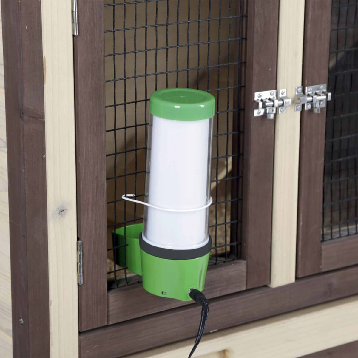 Ein grün-weißer Wasserspender ist an einem Holzkäfig befestigt. Der Käfig hat eine Maschendrahtfront und einen Metallverschluss.