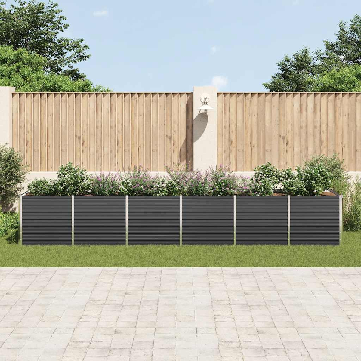 Eine Gartenszene zeigt einen dunkelgrauen Pflanzkübel mit Pflanzen vor einem Holzzaun. Im Vordergrund befindet sich eine Steinterrasse.