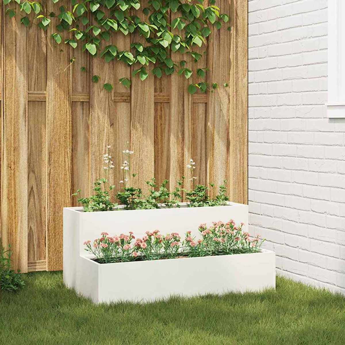 Una fioriera bianca a più livelli con fiori rosa e piante verdi è appoggiata sull'erba. Una staccionata di legno e un muro di mattoni bianchi fanno da sfondo.