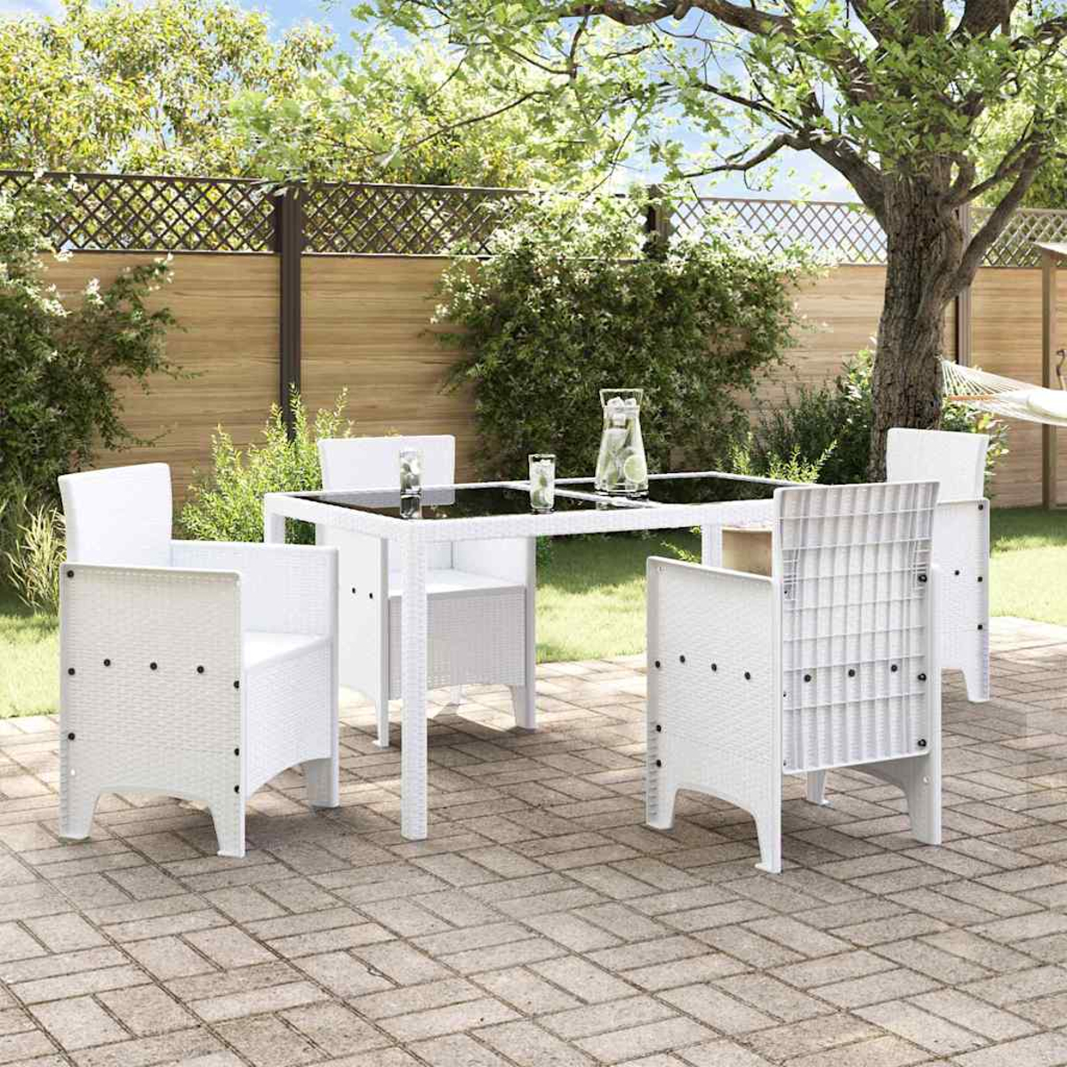 Ein weißes Ess-Set für den Außenbereich mit einem Tisch mit Glasplatte und vier Stühlen steht auf einer Ziegelterrasse mit Grün im Hintergrund.