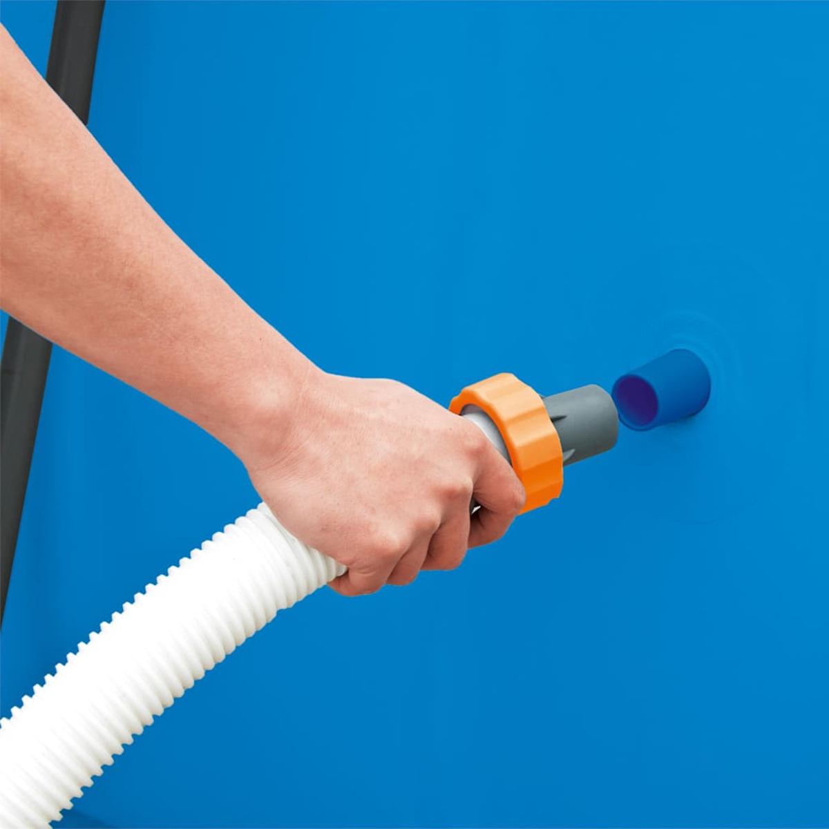 Eine Hand hält einen weißen Schlauch und verbindet ihn mit einer blauen Vorrichtung auf einer blauen Oberfläche. Ein orangefarbener Ring verbindet den Schlauch.