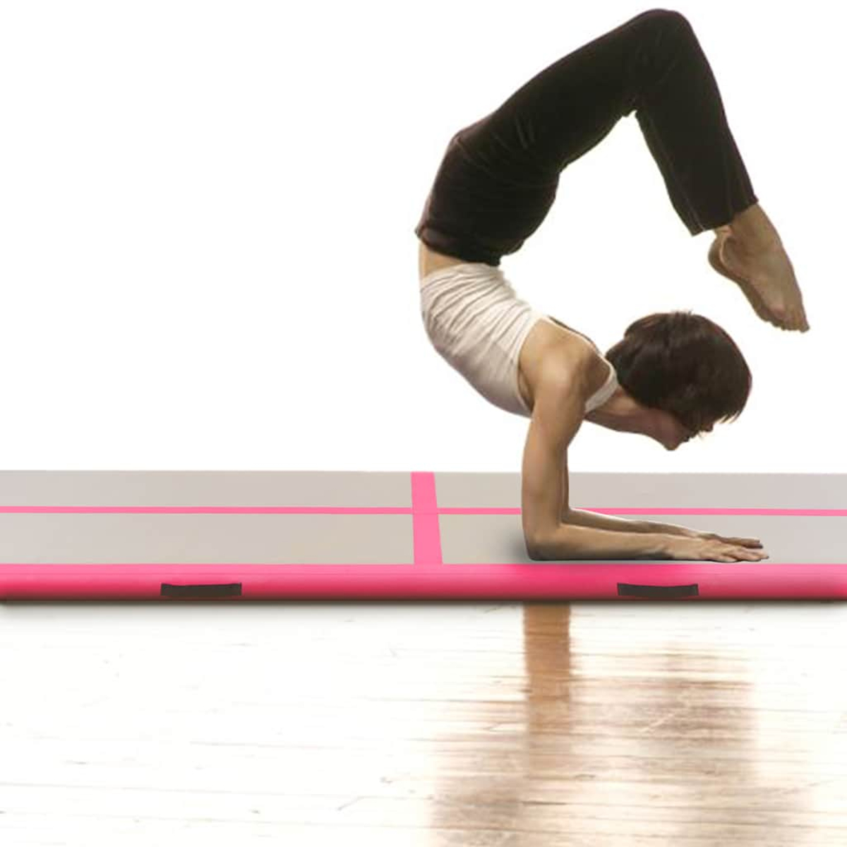 Eine Person macht einen Handstand auf einer Luftmatte. Sie trägt ein weißes Oberteil und eine schwarze Hose. Die Matte ist rosa und grau.