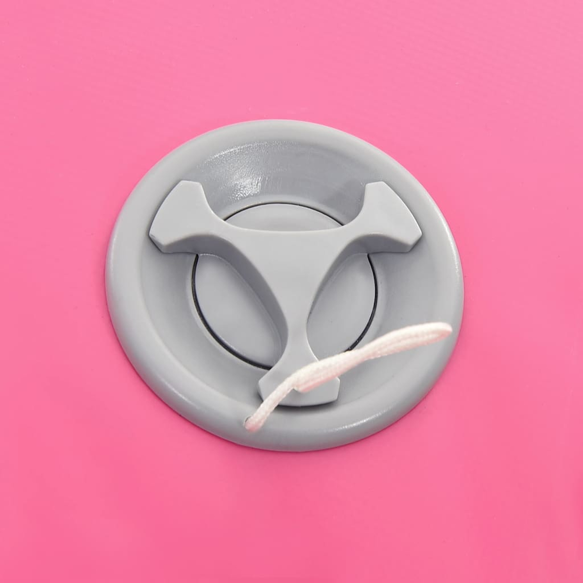 Una válvula gris con una cuerda blanca sobre una superficie rosa. La válvula tiene una manija de tres puntas. El fondo es rosa sólido.