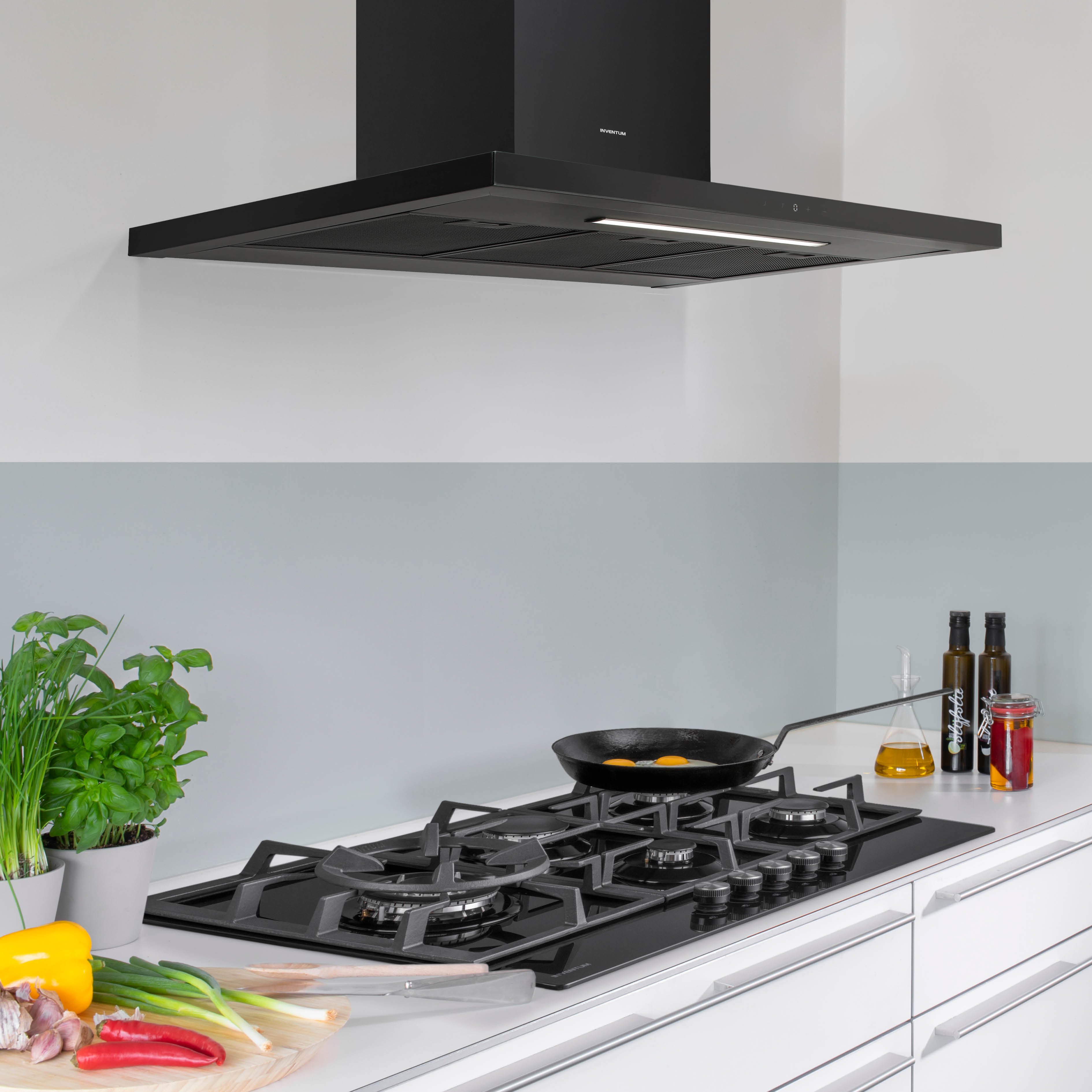 Kitchen scene with a black range hood, stove with eggs, vegetables, and oil bottles on a white countertop.