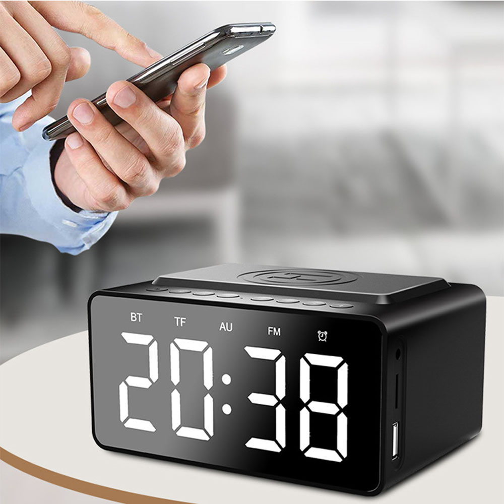 Eine Person benutzt ein Smartphone über einem schwarzen digitalen Wecker, der 20:38 anzeigt. Die Uhr hat eine kabellose Ladestation.