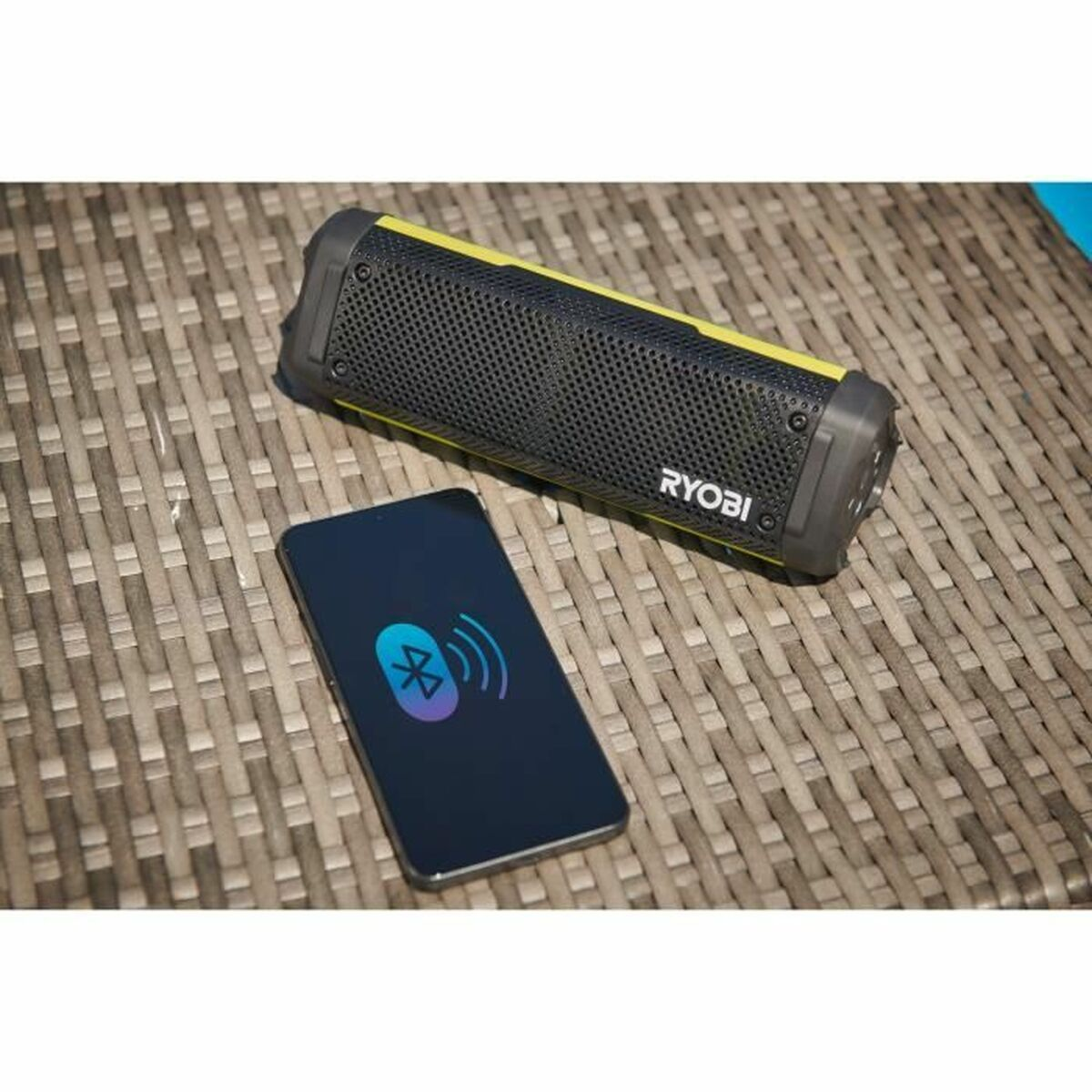 Un altoparlante Ryobi nero e uno smartphone con un simbolo Bluetooth su una superficie tessuta. Accenti gialli visibili sull'altoparlante.