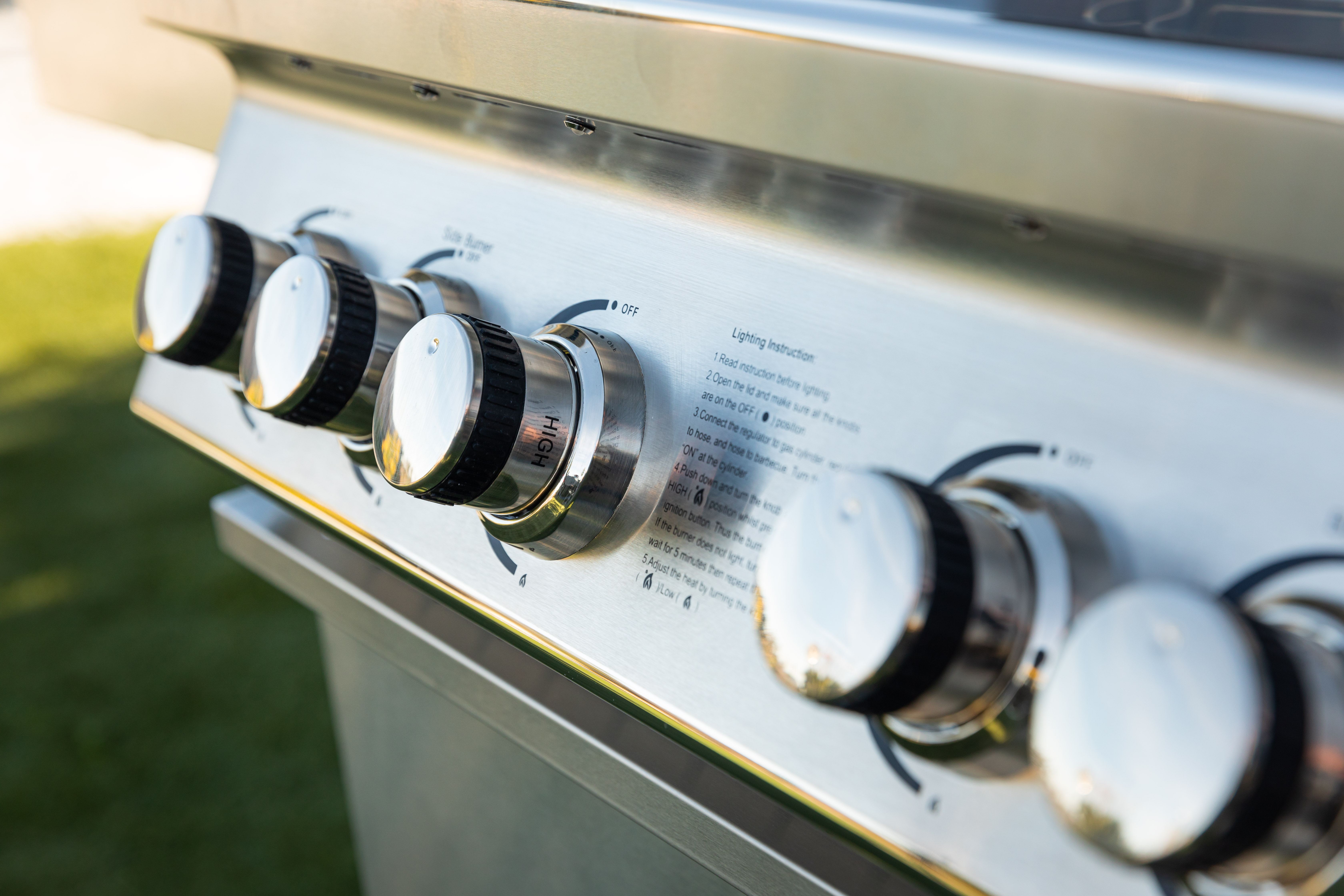 Primer plano del panel de control de una parrilla con perillas que dicen 'alto' y 'apagado'. Instrucciones para encender son visibles.