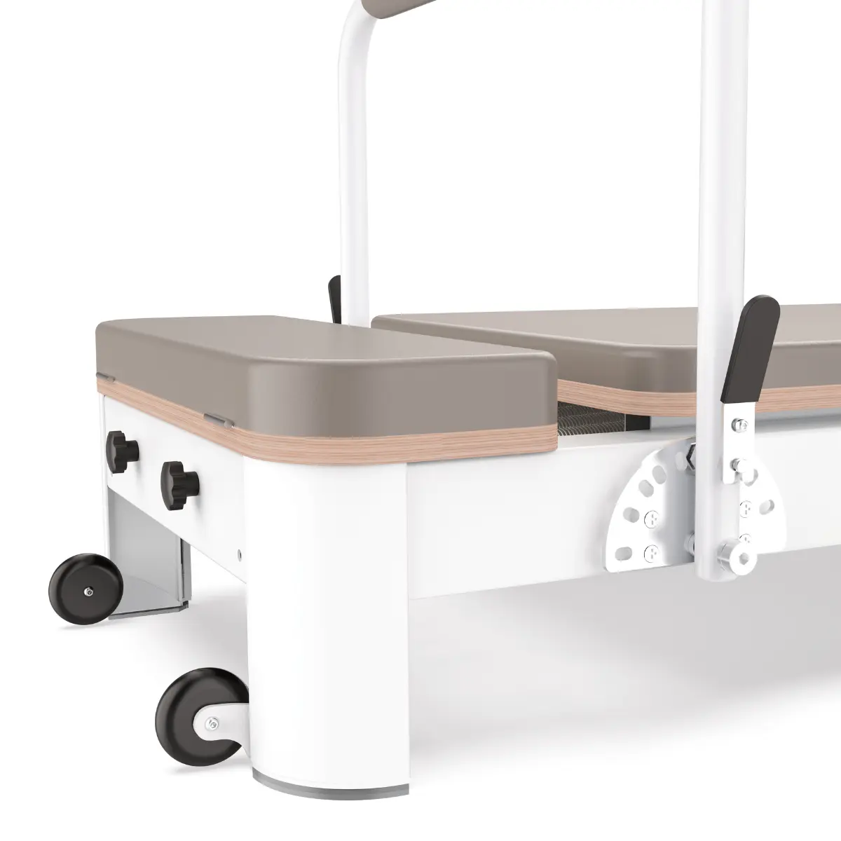 A pilates reformer machine. It has a white frame, wooden accents, gray cushions, and black wheels and handles.