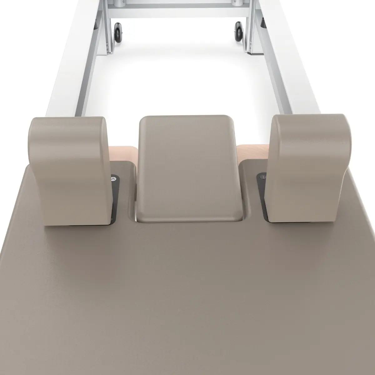 A Pilates machine with a gray padded surface, three padded headrests, and a white metal frame with wheels.