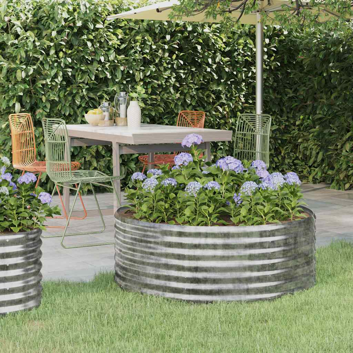 Szene im Freien mit Tisch, Stühlen und Metallpflanzgefäßen mit lila Blumen. Grüner Heckenhintergrund. Sonnenschirm und Sonnenlicht vorhanden.