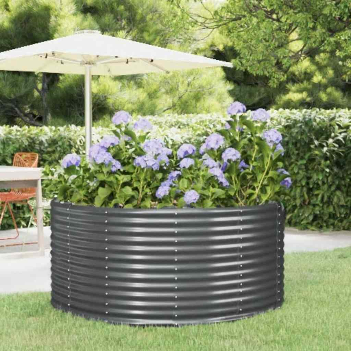 Ein Metallpflanzer mit lila Blumen unter einem weißen Sonnenschirm. Dahinter eine grüne Wiese und üppiges Laub.