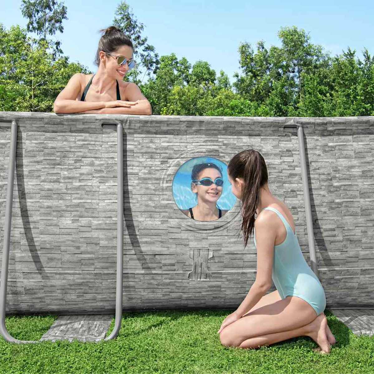 Zwei Frauen und ein Mädchen in einem Pool. Eine Frau schaut über die Mauer. Das Mädchen ist im Pool und schaut durch ein Fenster.