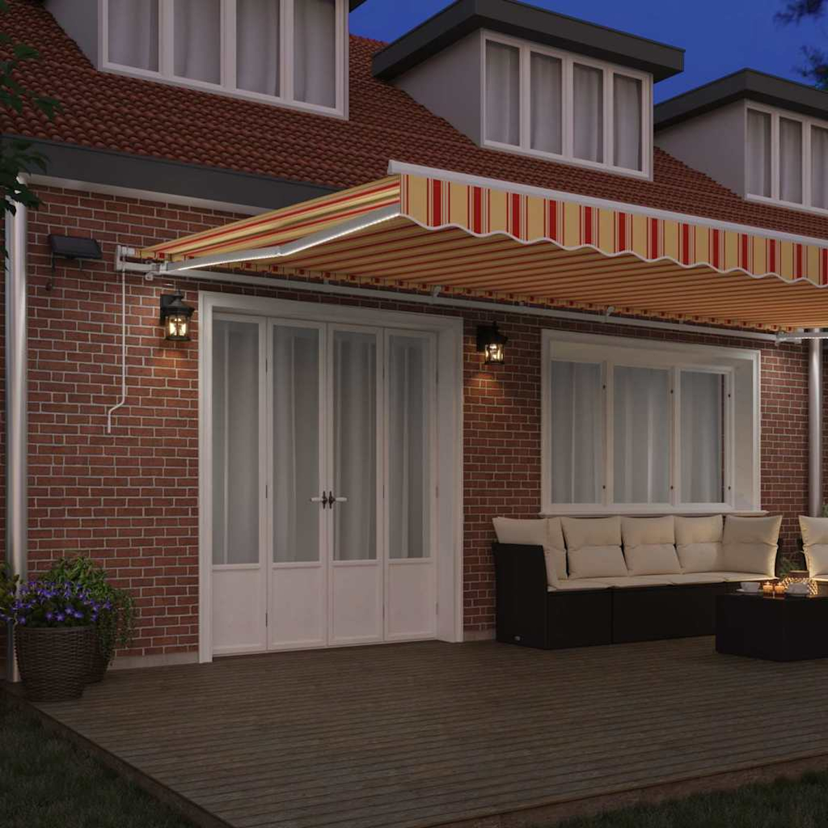Hausfassade in der Abenddämmerung. Ein gestreifter Baldachin bedeckt eine Terrasse mit Sofa und Tisch. Rote Backsteinmauer und weiße Türen.